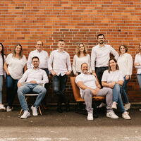 Das Team von Statik Maaß mit steht und sitzt vor einer rötlichen Backsteinwand.