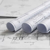 Nahaufnahme von Bauplänen auf welchen Wiederrum zusammengerollte Baupläne liegen.