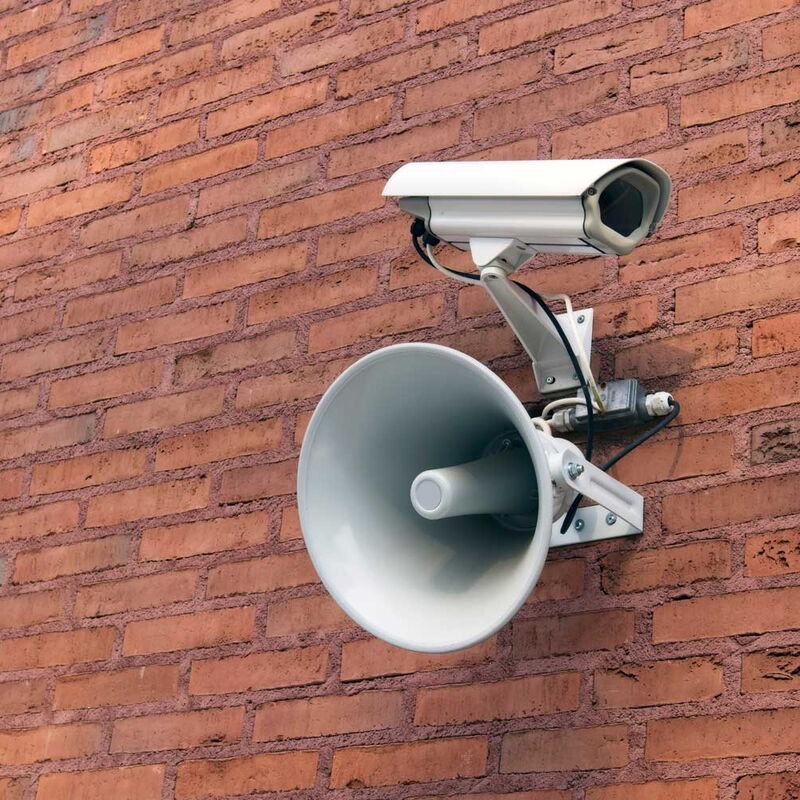 Lautsprecher und Kamerainstallation seitlich an einer rötlichen Backsteinwand installiert.