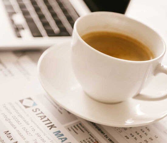 Kaffeetasse steht auf Zeichenplänen - im Hintergrund ist ein Laptop zu sehen.