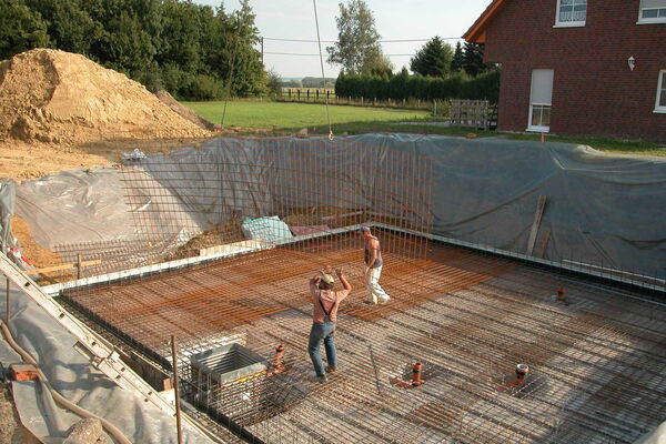 2 Bauarbeiter verlegen Stahlgitter in einer Ausschachtung, die mit Folien ausgelegt ist.